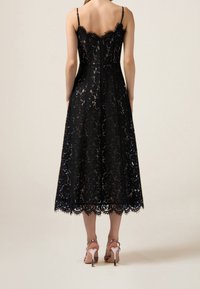 Robe en dentelle noire de longueur midi, avec un ourlet en forme de vague et des bretelles spaghetti ajustables. Caractérisée par un corsage ajusté et un délicat motif floral.