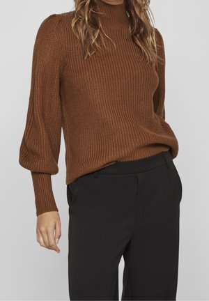 Pull marron en maille côtelée avec un col montant et des manches bouffantes, associé à un pantalon noir ajusté. Texture lisse et coupe cintrée.