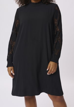 Robe noire avec des manches longues en dentelle, col rond et poignets froncés. Corps en tissu lisse avec une coupe ample, design arrivant au genou.