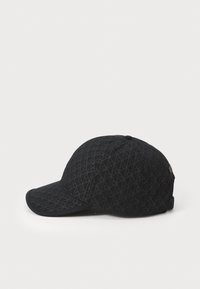 Black cap with a textured pattern featuring interlocking shapes. Curved brim and adjustable strap at the back. Soft fabric material.