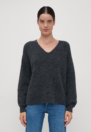 Tamno siva, teksturirana pletiva sa V-izrezom, oversize krojem i dugim rukavima. Uparena s plavim trapericama. Koristeni su mekani, pahuljasti materijali.