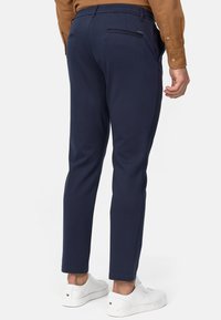 Pantalones ajustados azul marino en tejido suave con un acabado pulido, que cuentan con detalles de bolsillo trasero y se combinan con zapatillas blancas.