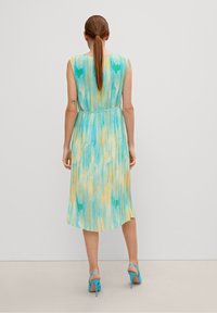 Ärmelloses Kleid in blau, grün und gelbem Batikmuster. Verfügt über eine plissierte Textur und eine taillierte Taille mit einem ausgestellten Saum. Kombiniert mit blauen High Heels.
