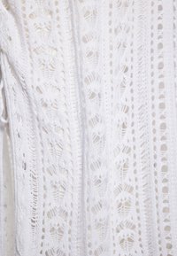 Weißes Strickoberteil mit aufwendigen offenen Mustern, strukturiertem Finish und vertikalen Streifen im gesamten Stoff.