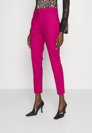 Slim-fit felroze enkellange broek gedragen met zwarte schoenen met spitse neus en een zwart kanten top met lange mouwen.