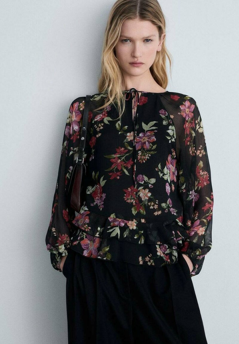 Blusa nera trasparente con motivo floreale nei toni di rosso, rosa e verde, dotata di scollatura rotonda, orlo volants e maniche lunghe a palloncino.