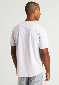 Jasnolavendowa koszulka z krótkim rękawem wykonana z bawełny, z zaokrąglonym dołem i detalem na plecach. Gładka struktura z podwiniętymi krawędziami rękawów.