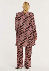 Patroonsuit met een lange jas en wijde broek in zwart, rood en witte cirkelvormige ontwerpen. Gladde stof met een op maat gemaakte pasvorm.