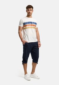 White short-sleeve T-shirt with blue, orange, and yellow horizontal stripes; paired with navy cropped pants; white sneakers.