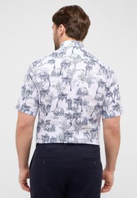 Korte mouw shirt in het wit met een blauw tropisch motief van palmbomen, hutten en zeilboten. Met kraag en een relaxte pasvorm.