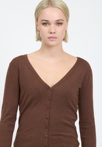 Cárdigan marrón de mangas largas, hecho de tejido de punto suave, con un escote en V y una fila de seis botones marrones en la parte delantera.
