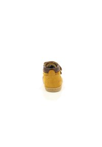 Zapato infantil de ante marrón y amarillo con punta redondeada, tira de velcro y collar acolchado en el tobillo. Suela de goma color beige claro.
