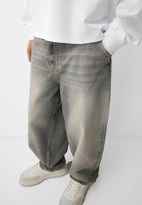 Loose-fit grey denim jeans with a faded finish and light distressing; features side pockets and a stitched waistband detail.