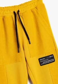 Gelbe Sweatpants mit strukturierter Oberfläche, elastischem Bund und schwarzen Kordelzügen. Verfügt über aufgesetzte Taschen und ein Markenlabel.