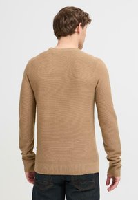 Suéter marrón de punto con escote redondo y mangas largas. Presenta puños y dobladillo acanalados, mostrando una tela suave y texturizada.
