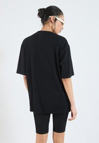 Camiseta negra de gran tamaño, de manga corta, de material de algodón, con diseño liso. Usada con pantalones cortos de ciclismo negros, de textura suave, con detalles mínimos.
