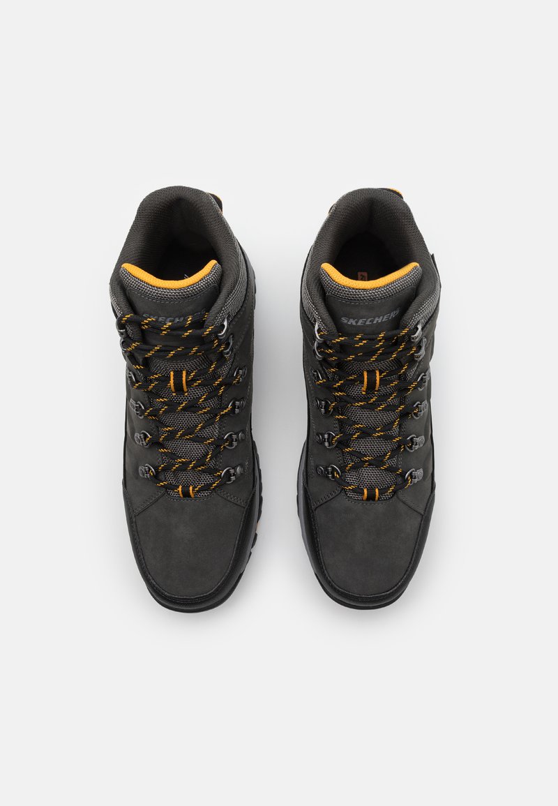 Botas de senderismo negras fabricadas en ante y malla, con acentos naranjas, un sistema de cordones robusto y soporte alto para el tobillo, diseñadas para ser duraderas.