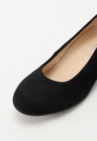 Bailarinas de ante negro con puntera redondeada. Textura suave, diseño minimalista y suela delgada. Forro interior visible. Indicador de talla presente.
