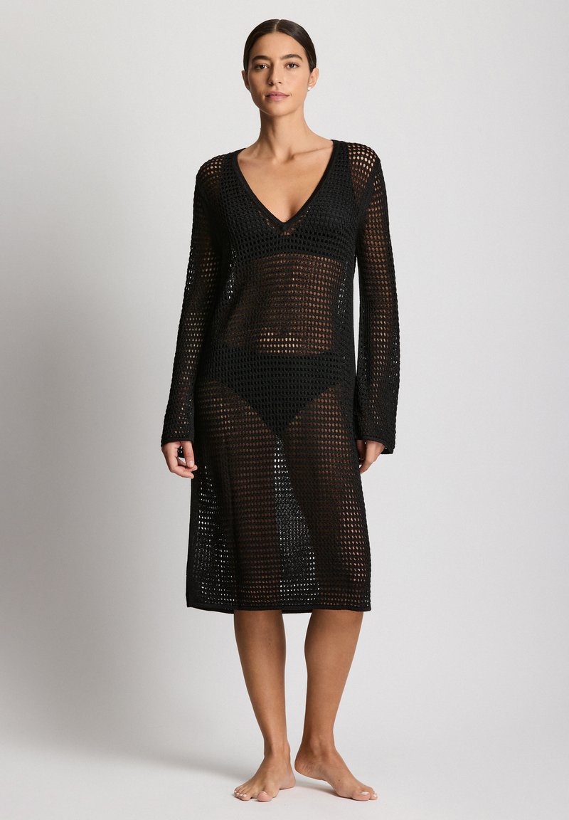 Fekete hálós takaróruha hosszú ujjakkal és V-nyakkivágással. Laza kötött textúrával, közép-vádli hosszúsággal és átlátszó kialakítással.