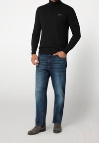 Schwarzer Rollkragenpullover im figurbetonten Stil, kombiniert mit blauen Jeans im geraden Schnitt. Graue Wildleder-Ankle Boots runden das Outfit ab.
