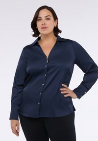 Námořnická modrá saténová košile na knoflíky s límcem, dlouhými rukávy a detaily ve tvaru klíčové dírky na dekoltu. Obsahuje lesklé knoflíkové zapínání.