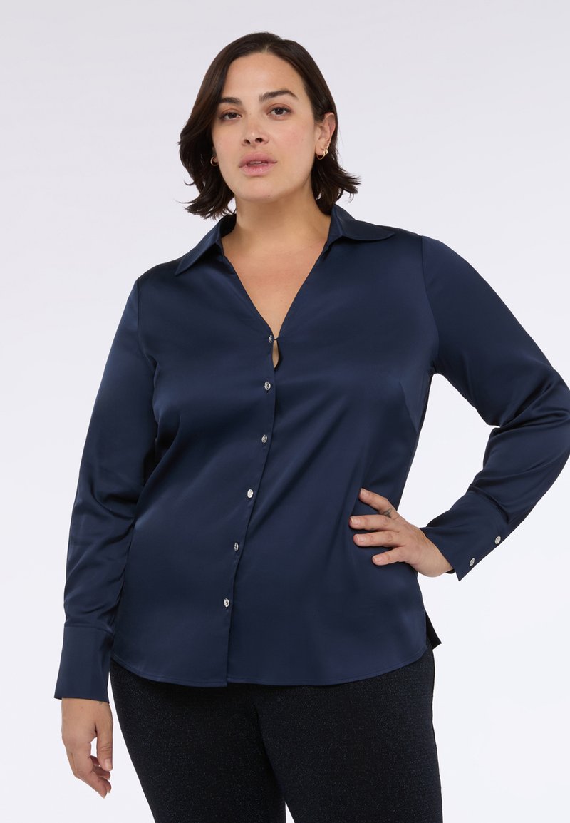 Námořnická modrá saténová košile na knoflíky s límcem, dlouhými rukávy a detaily ve tvaru klíčové dírky na dekoltu. Obsahuje lesklé knoflíkové zapínání.