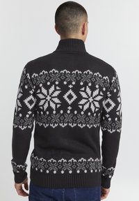 Gestrickter Pullover in Dunkelgrau mit einem weißen Schneeflocken- und geometrischen Muster. Verfügt über einen hohen Kragen und gerippte Säume für einen strukturierten Abschluss.
