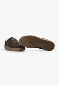 Bruna mockaskor med en texturerad gummisula, med snörning fram och krämfärgade accenter. Logotyp på sidan, diamantmönstrad yttersula.