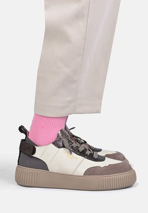 Fod iført beige bukser, lyserøde sokker og en sneaker med hvide, sorte og brune toner, tykk sål og snørelukning.