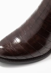 Botín oscuro de cuero brillante con patrón de cocodrilo, con punta redondeada y suela texturizada con borde cosido.