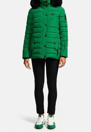 Groene gewatteerde jas met een faux fur capuchon, ritszakken aan de zijkant en zwarte drukknoopjes. Draagt over zwarte broeken en sneakers met groene accenten.