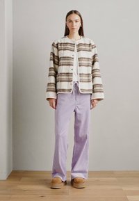 Ullblandingjakke med brune striper, rund halslinje og knapper; kombinert med lyse lilla stripete bukser og brune slip-on sko på et tregulv.