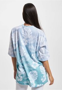 Camiseta de gran tamaño en azul claro con patrones blancos de flores y hojas. Hecha de material suave con un ajuste cómodo. Mangas cortas y escote redondo.
