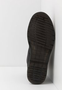 Černá gumová podešev boty s texturovaným vzorem pro lepší přilnavost. Má zaoblenou špičku a hladké hrany, s vyraženou značkou blízko paty.