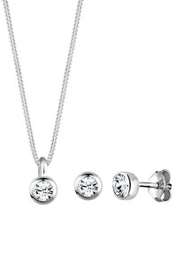 Collana d'argento con un pendente circolare e orecchini a perno coordinati, caratterizzati da gemme trasparenti in montature lucide.