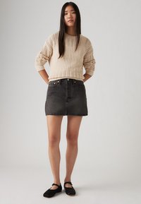 Pull en tricot beige avec un motif texturé, associé à une mini-jupe en denim noir et des chaussures noires de style Mary Jane. Tenue décontractée.