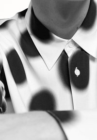 Hemd mit durchgehender Knopfleiste und einem schwarz-weiß gepunkteten Muster; aus glattem Stoff gefertigt, mit spitzem Kragen und weißen Knöpfen.