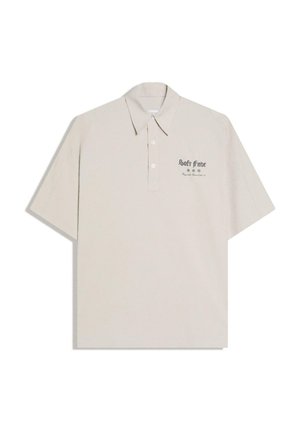 Polo beige à manches courtes avec col et boutons, avec texte noir et petits symboles sur la zone gauche de la poitrine.