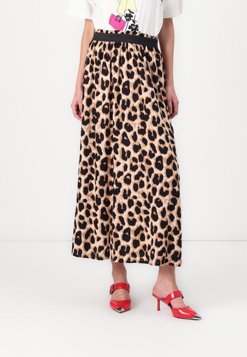 Maxiskjørt med leopardmønster og svart elastisk linning; stoffet er glatt og lett. Kombinert med røde høyhælte sko med metalliske detaljer.