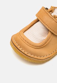 Brune lærskot med rund tå og Velcro-lås. Har synlig søm og en teksturert innersåle, hviler på en myk gummiyttersåle.