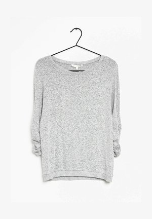 Szara bluzka z długim rękawem o luźnym kroju, z szerokim dekoltem, teksturowaną tkaniną i podwiniętymi rękawami. Zawieszona na czarnym haczyku.