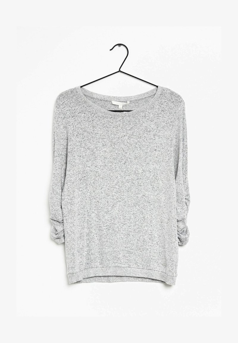 Szara bluzka z długim rękawem o luźnym kroju, z szerokim dekoltem, teksturowaną tkaniną i podwiniętymi rękawami. Zawieszona na czarnym haczyku.