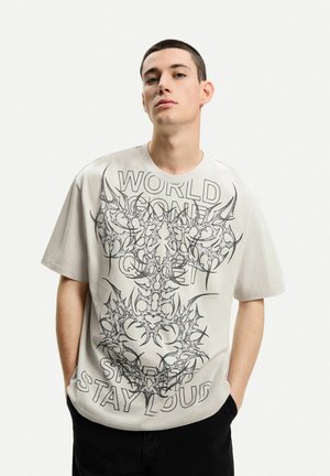 T-shirt in cotone grigio chiaro con design grafico nero bold che presenta motivi intrecciati e testo: "WORLD", "QUIET", "STAY LOUD". Maniche corte.