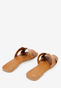 Sandali piatti marroni con punta aperta e design con cinturini incrociati, caratterizzati da una texture in similpelle liscia e suola in gomma resistente.