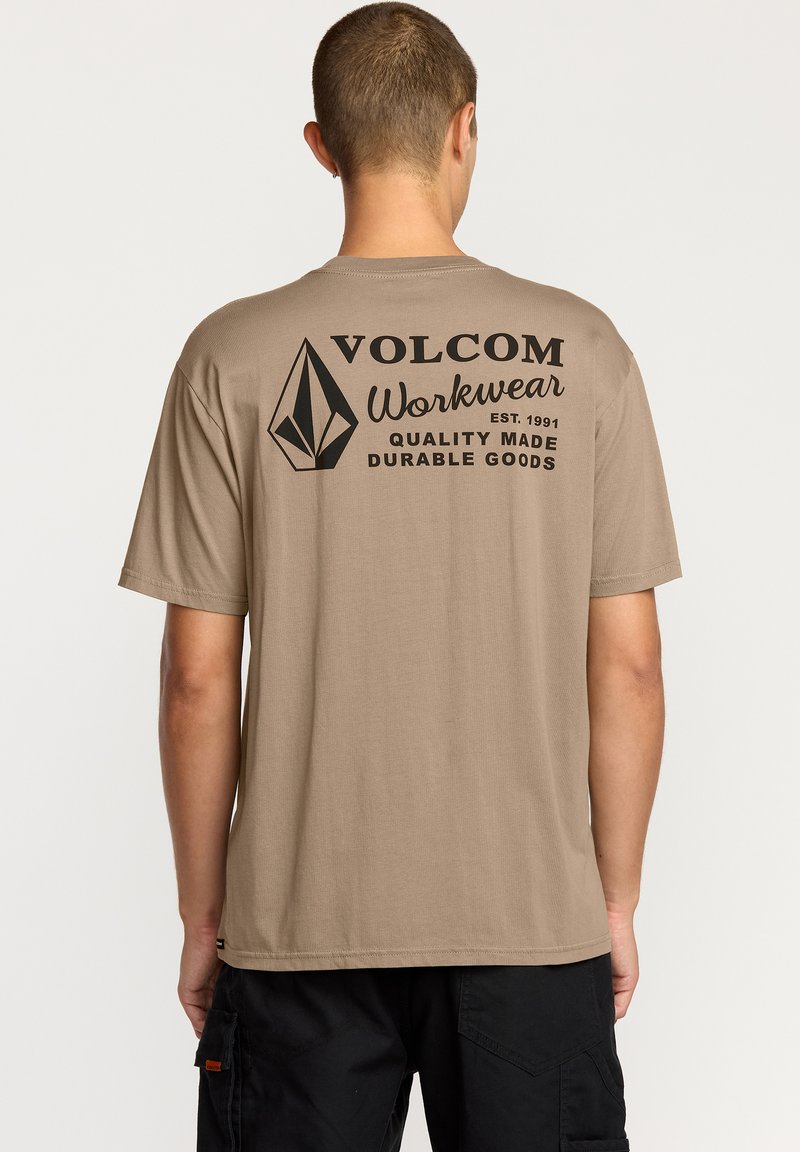 T-shirt en coton beige avec un col rond, featuring une impression graphique noire au dos, comprenant un logo en diamant et du texte.