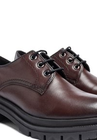 Zapatos de cuero marrón con un acabado suave, forma de punta redondeada, cordones negros y una suela de goma negra gruesa con un patrón texturizado.