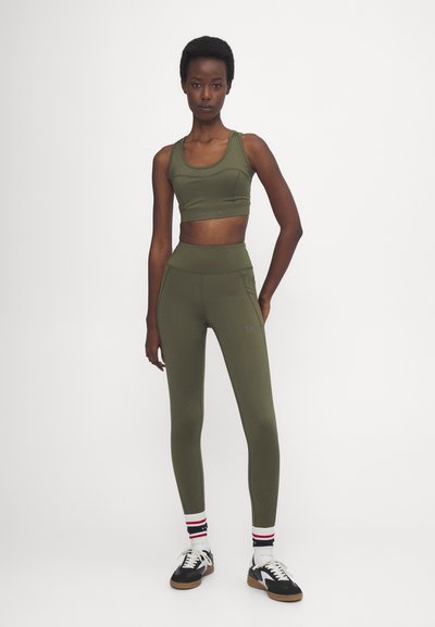 Olivově zelený sportovní crop top a legíny s vysokým pasem vyrobené z elastického materiálu, doplněné černobílými teniskami a pruhovanými ponožkami.