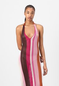 Strikket halterneck-kjole med vertikale striper i rosa, brun og krem, med en dyp V-hals og en liten logo-akseent på brystet.