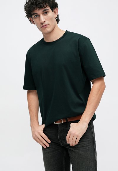 Tricou scurt din bumbac de culoare verde închis, purtat cu blugi negri și o curea maro. Croială casual și decolteu tip Crew.