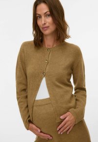 Brun strikket cardigan med rund hals, tre knapper og åpning foran. Myk tekstur, kombinert med en hvit innertrøye og matchende underdel.